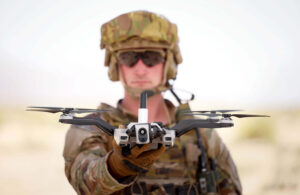 A solder in camo and sunglasses looking into the camera and holding Red Cat's Black Widow drone.