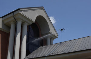 A Lucid Bots drone spraying water at the window of a school.