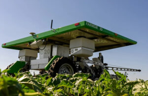 An image of the FarmDroid FD20, which looks like a wide, flat platform with green edges on top of a tractor-like system.