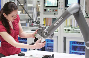 A woman in a red shirt with dark hard operating an Omron cobot.