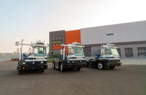 Three autonomous Outrider yard trucks outside of an Outrider facility.