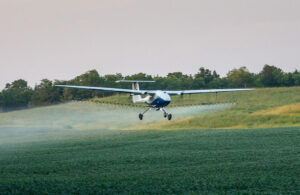 A white Pyka aircraft flying flow and spraying crops.