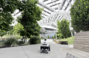 A black and white mobile robot using ReMEmbR rolling along a sidewalk with trees on both sides.