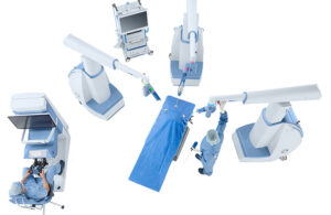 A bird's eye view of Asensus Surgical's Senhance Surgical System, featuring three long robotic arms hovering over an empty hospital bed and a control station.