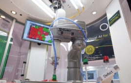 A grey Stäubli SCARA robot with a green suction cup end effector picking a hamburger patty using Oxipital AI's software.