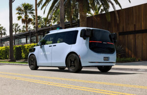 Waymo's sixth generation autonomous vehicle driving down a road with palm trees in the background.