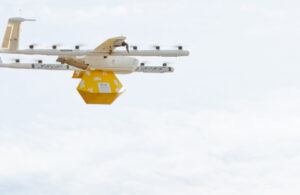 A Wing Aviation drone carrying a yellow package through the sky with FAA BVLOS certification.